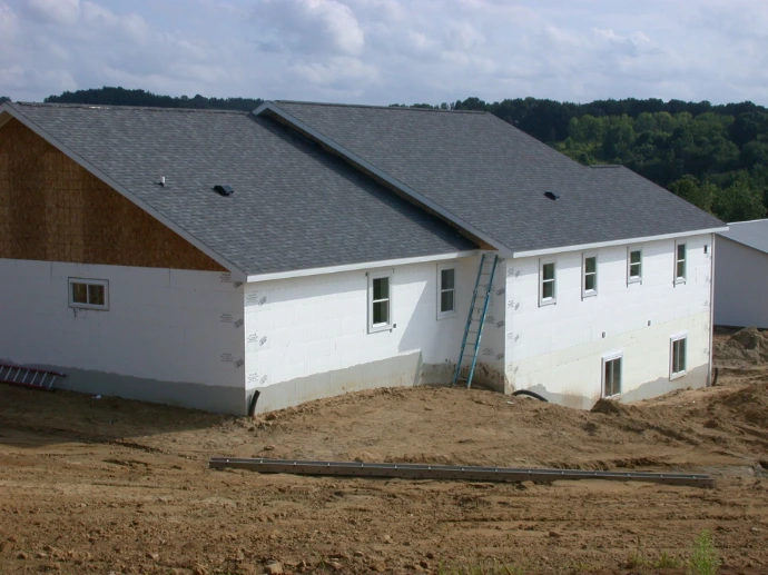 A finished home with a gray shingle roof and white CelBlox ICF walls, trees in the background.