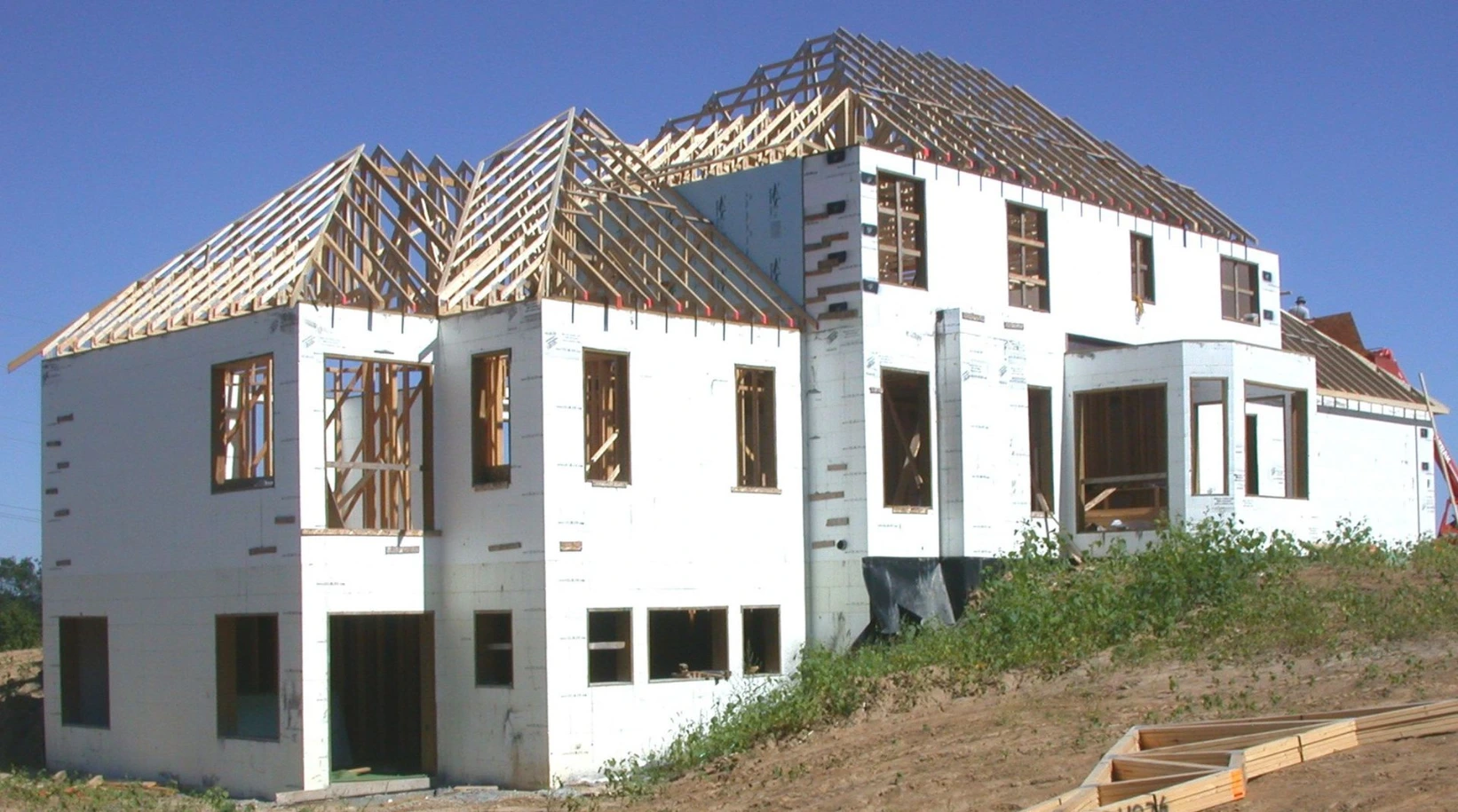 Multi-story residential home partially constructed with CelBlox ICF blocks. The white insulated concrete form walls are up with window openings framed, and the wood roof trusses are being installed under a clear blue sky.