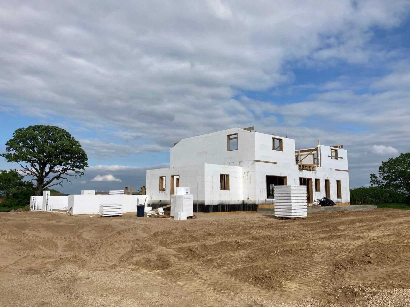 A residential ICF home under construction in Wisconsin, with white insulated concrete form walls on the first floor and wood framing for the second story, an oak tree and farmland in the background.