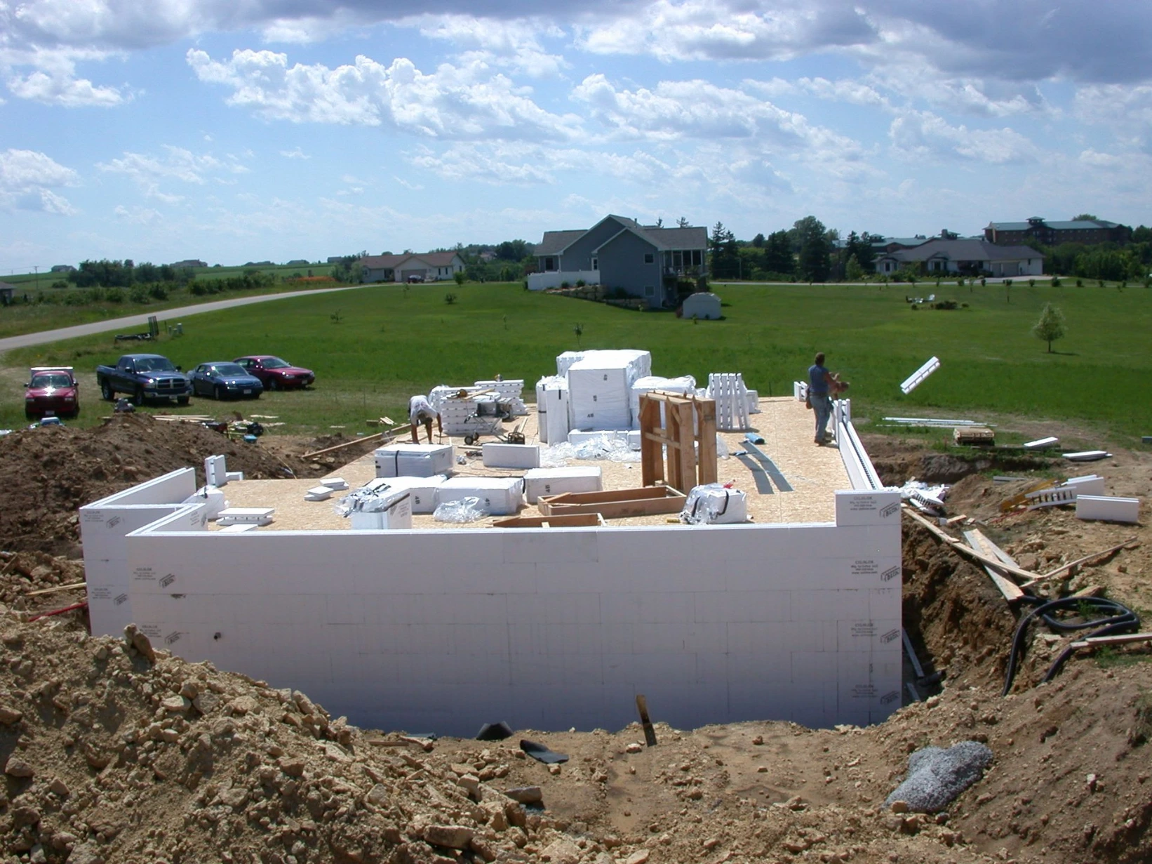 Freshly formed ICF foundation walls for a residential build, with pallets of CelBlox insulated concrete forms staged on site and a rural neighborhood in the background.