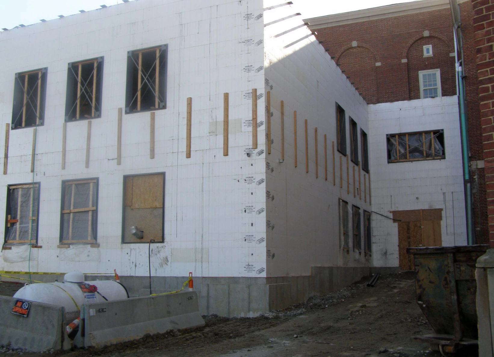 Commercial ICF building addition under construction next to an existing brick building, with white insulated concrete form walls, scaffolding, and framed window openings.