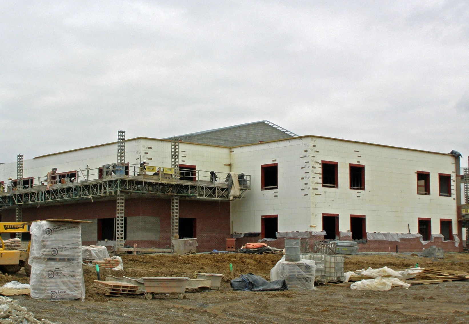 Long commercial ICF building with a completed metal roof, white insulated concrete form walls, red door and window frames, and scaffolding still in place.