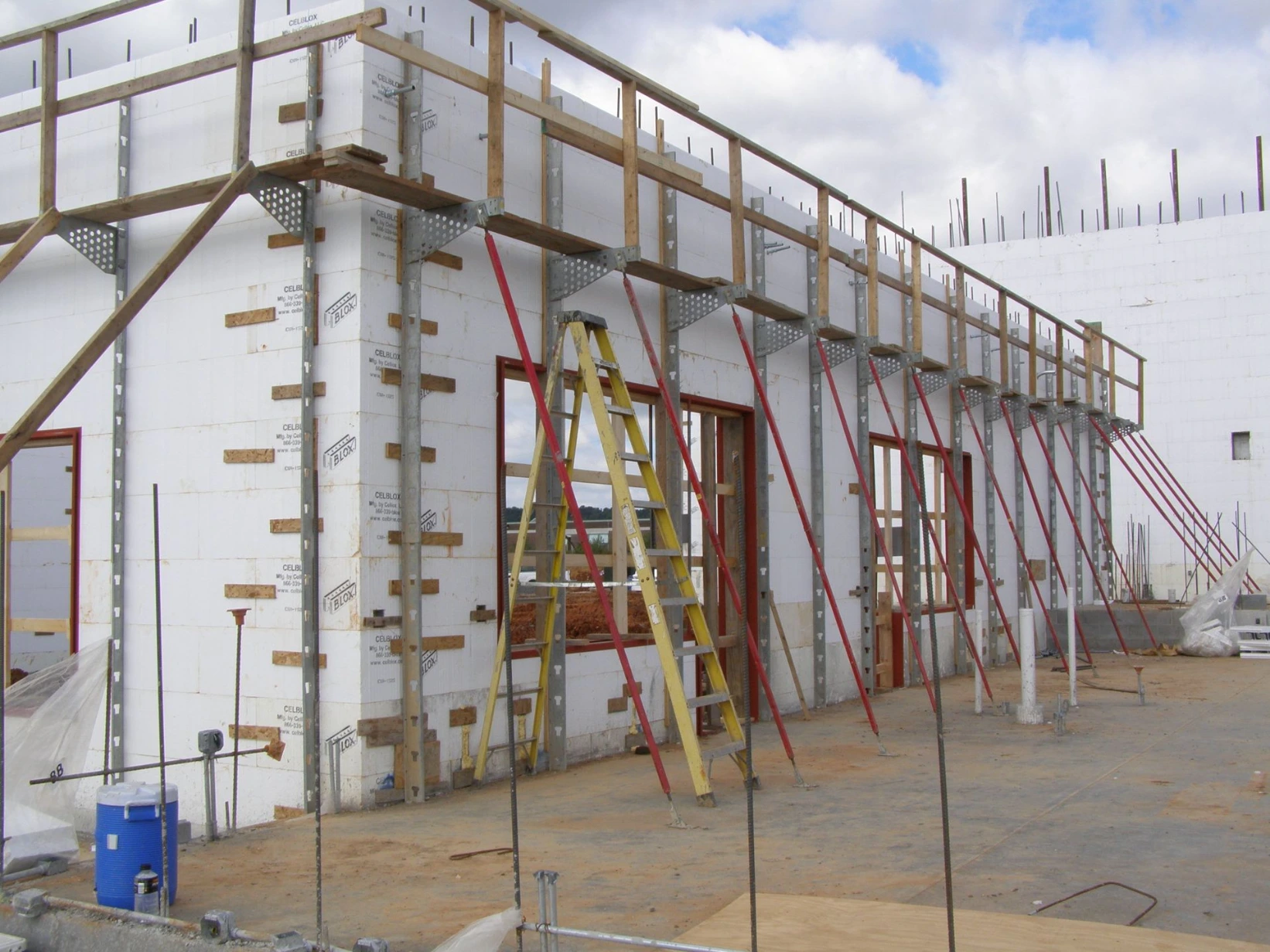 Tall commercial ICF wall for the Flaherty School project, braced with a red scaffold bracing system and yellow ladder for access.