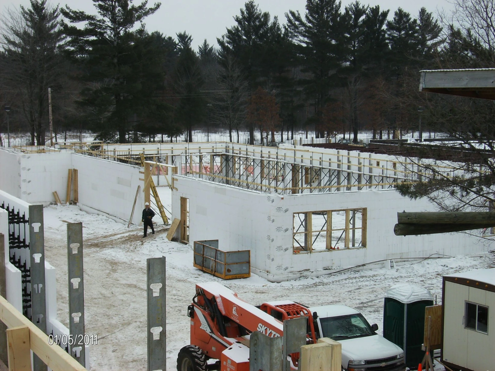 Aerial view of an L-shaped commercial ICF building foundation in the snow, with white insulated concrete form walls, scaffolding, and a worker on site.