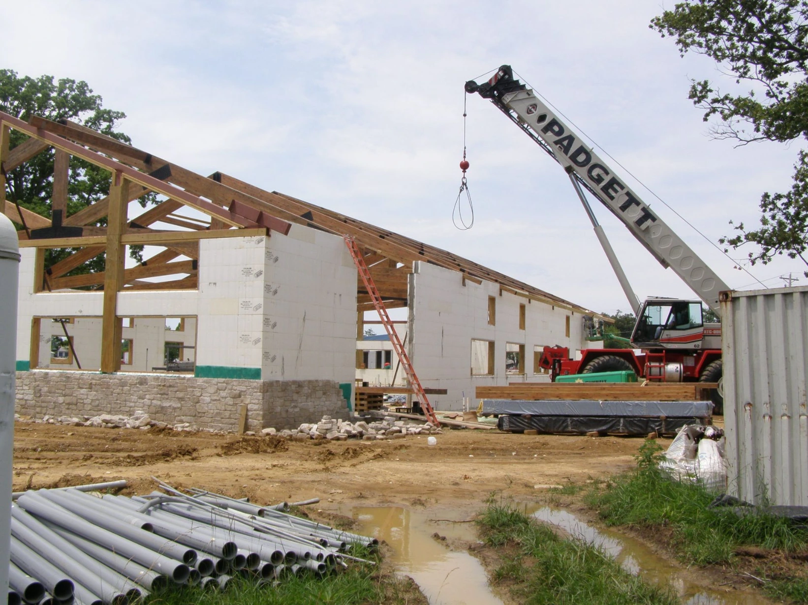 Commercial ICF building with wood roof trusses being hoisted into place by a mobile crane above white insulated concrete form walls.