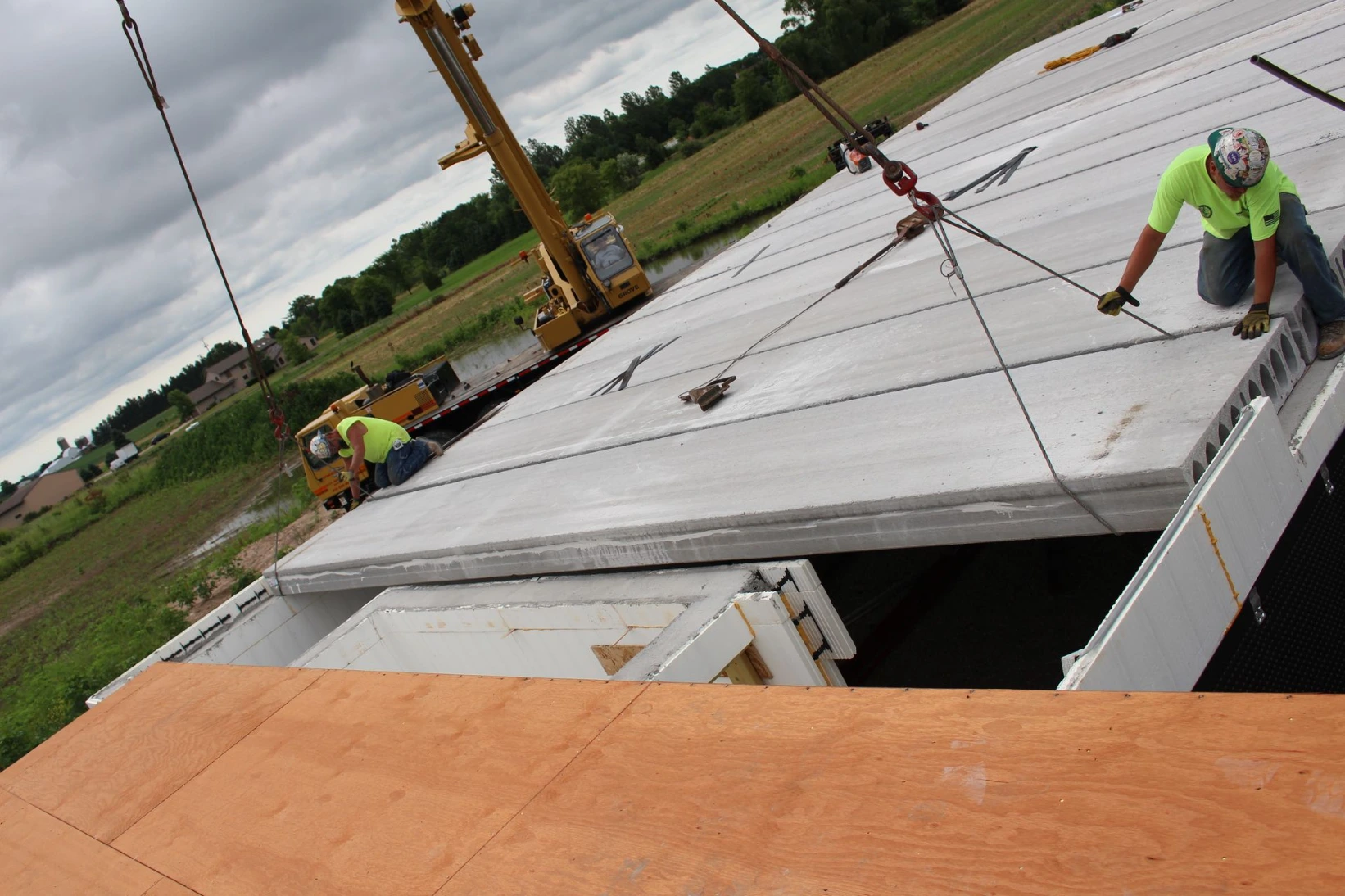 Worker finishing a large poured concrete floor slab inside a commercial ICF building, with a crane and equipment staged in the background.